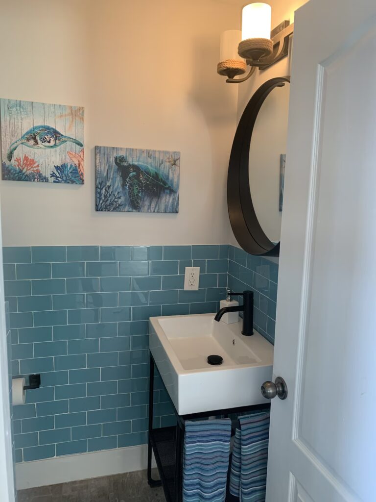 Compact powder room at Indigo House Exuma with a round mirror, modern fixtures, and teal backsplash tile.