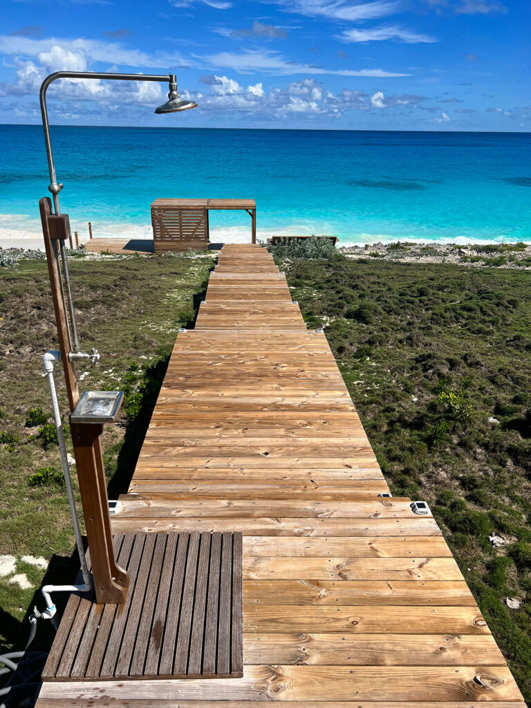 Wooden boardwalk leading to a white sand beach and vibrant turquoise Exuma ocean.