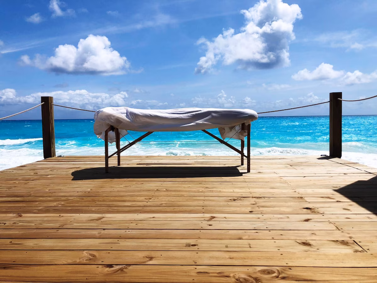 Indigo-House_concierge-1_1200 Massage table on a wooden deck overlooking the ocean in Exuma, perfect for beachfront spa treatments.