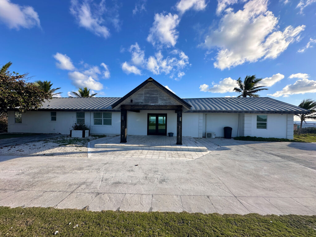Ground-level view of Indigo House Exuma showing the driveway and main entrance with bright blue sky overhead.