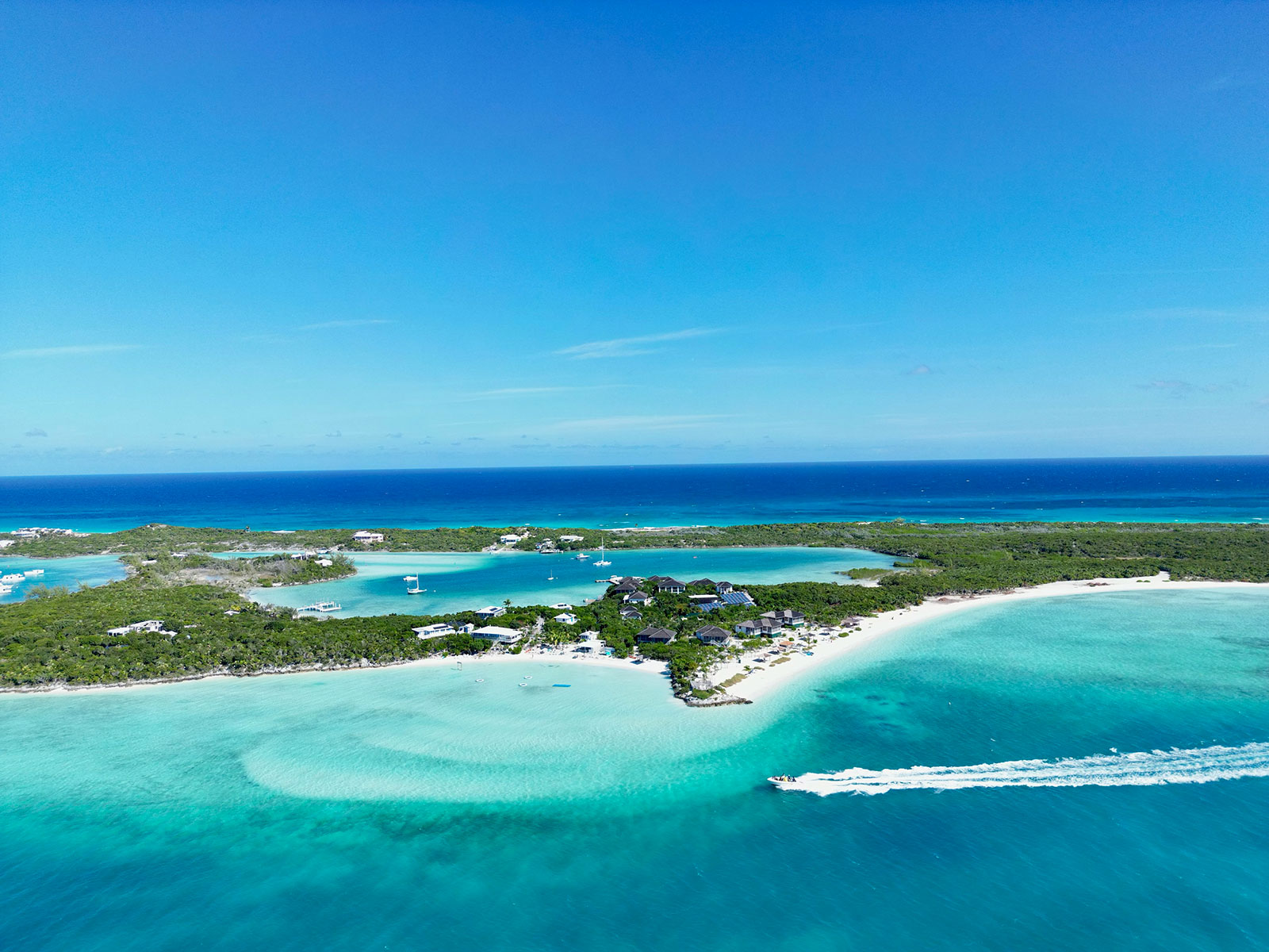 Indigo-House_exuma-1_1600 Aerial view of a tropical island in Exuma surrounded by turquoise water, white sand beaches, and boats near the shoreline.