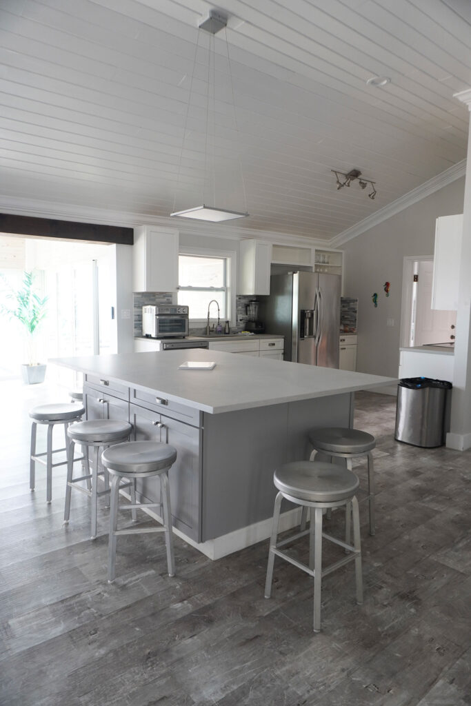 Spacious kitchen at Indigo House Exuma with a large island, barstools, and gray flooring.