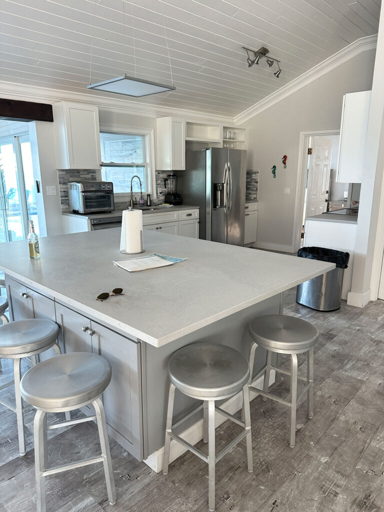 Bright kitchen at Indigo House Exuma featuring a large island with barstools, stainless steel appliances, and coastal decor.