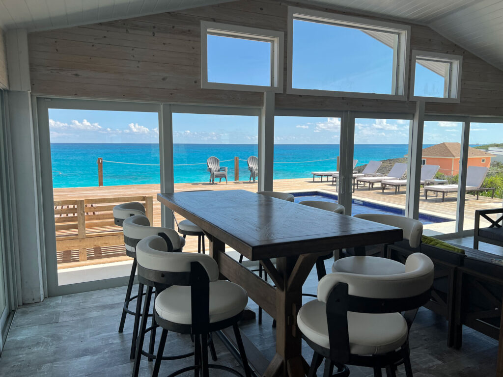 Dining space at Indigo House Exuma with panoramic ocean views through floor-to-ceiling windows.