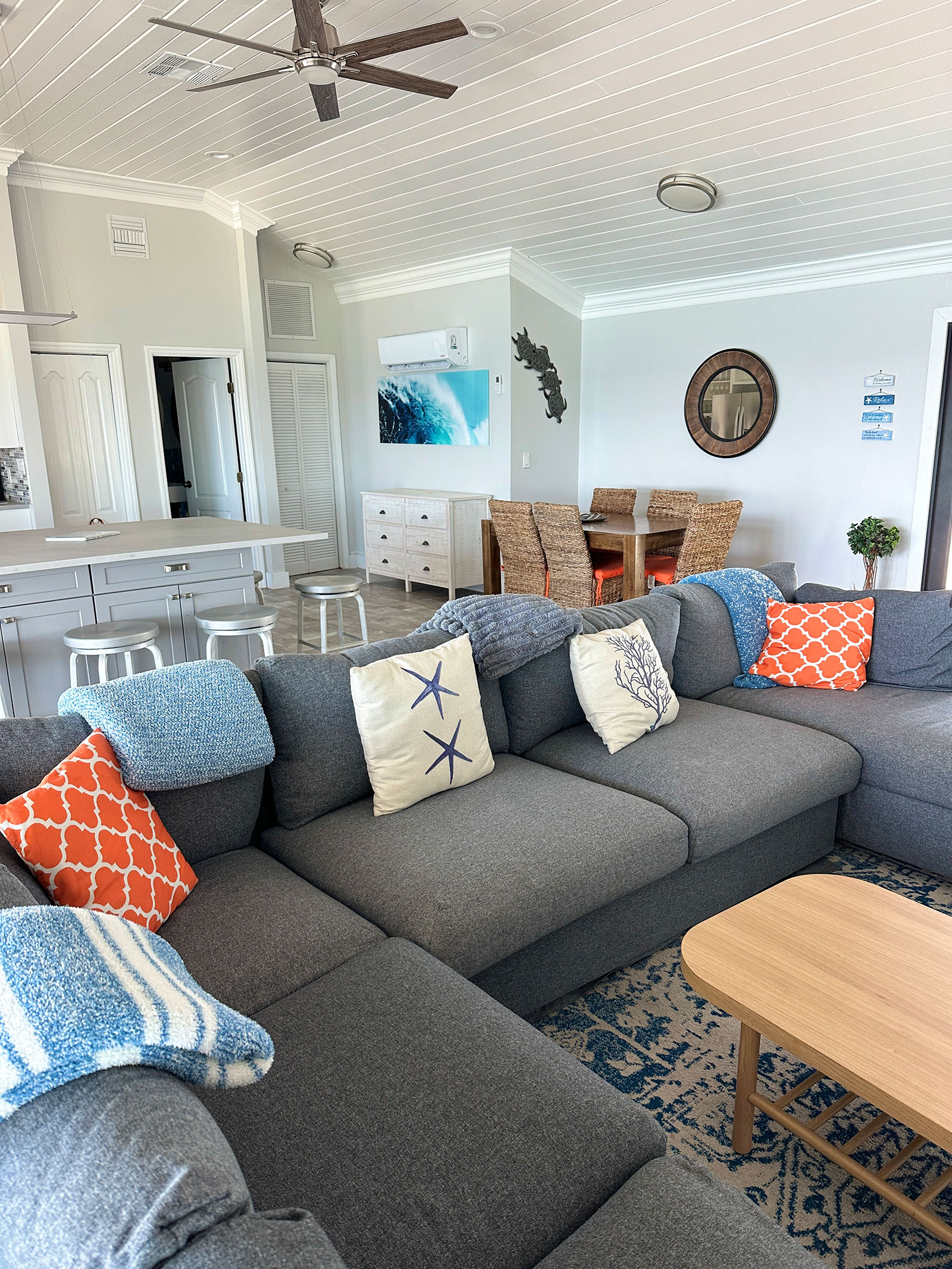 Indigo-House_living-4_1600 Coastal-themed living area at Indigo House Exuma featuring a large gray sectional, woven dining chairs, and beach-inspired decor.