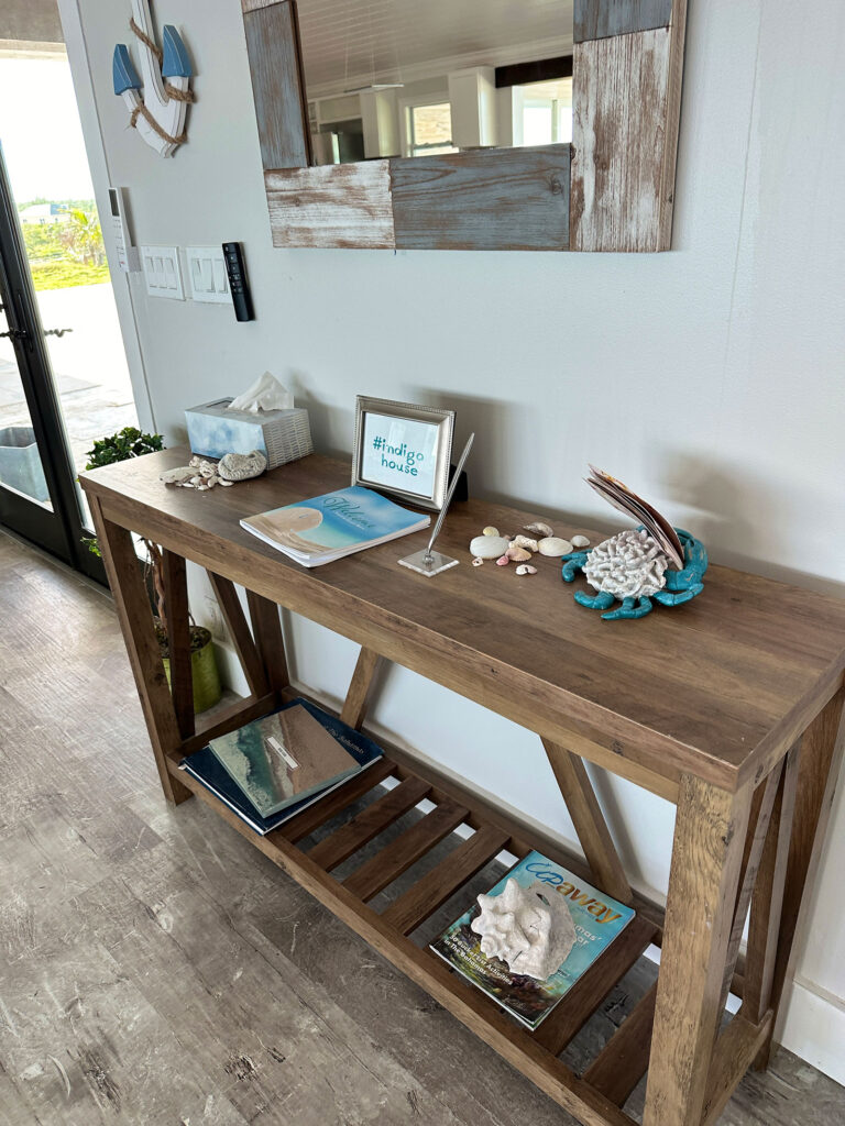Beach-inspired console table at the entry of Indigo House Exuma with seashells and welcome materials.