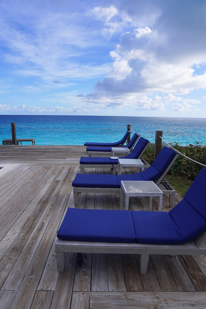 Row of cushioned blue loungers on the oceanfront deck at Indigo House Exuma with uninterrupted sea views.
