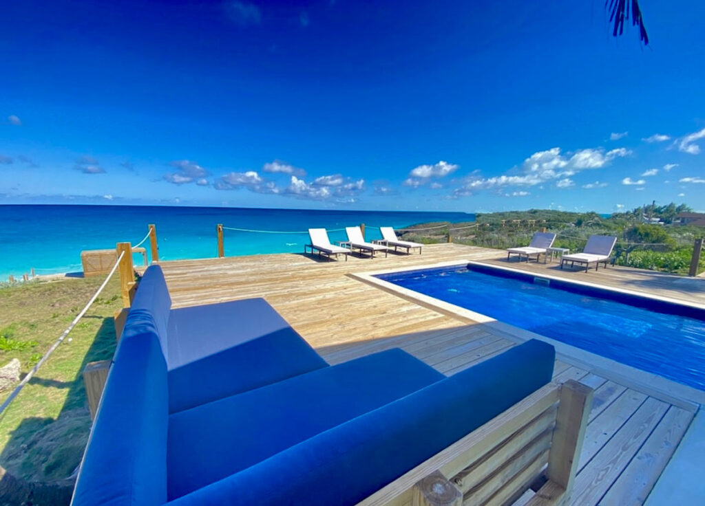 Heated pool and lounge chairs at Indigo House Exuma overlooking the turquoise sea and clear blue skies.