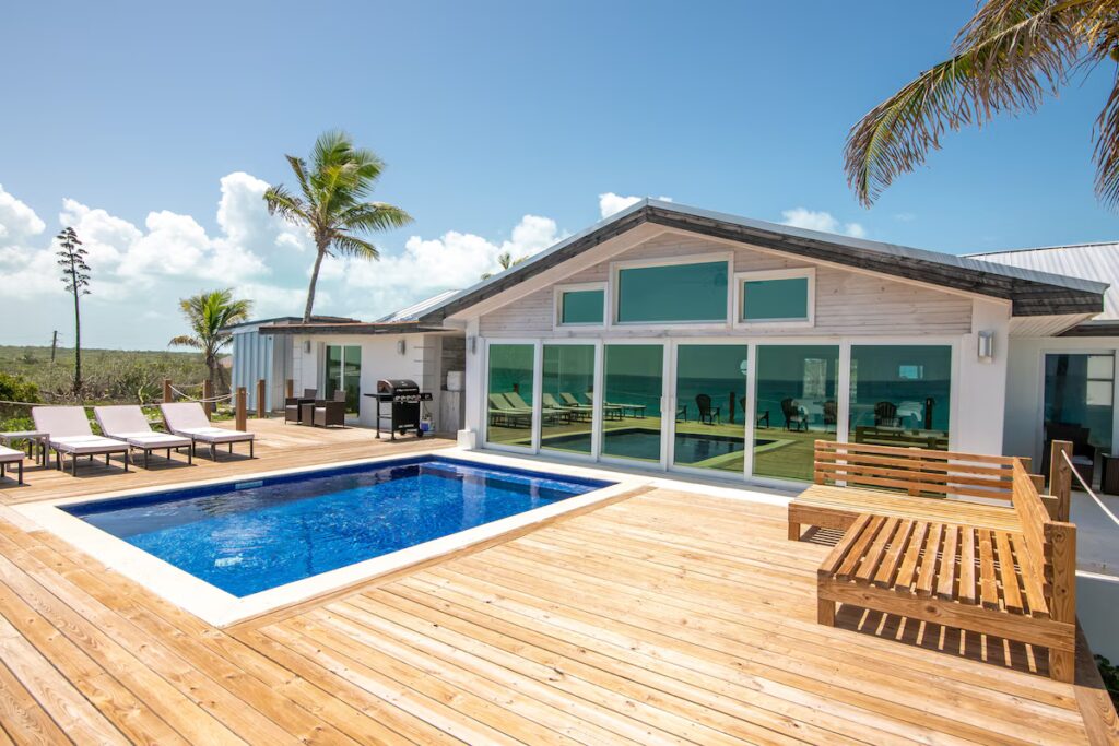 Private pool and sundeck at Indigo House Exuma with palm trees and modern villa facade in the background.