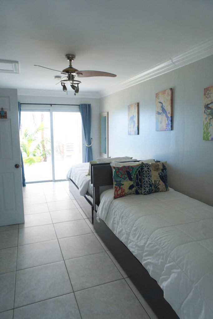 Guest bedroom at Indigo House Exuma with twin beds, ocean view, and sliding door access to the outdoors.